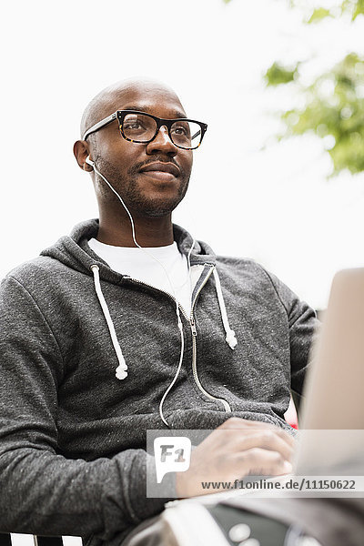 Schwarzer Mann mit Laptop und Kopfhörern im Freien