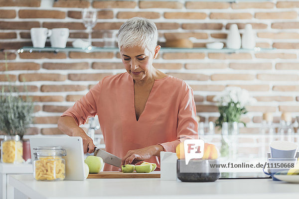 Older Caucasian woman cutting apples in kitchen