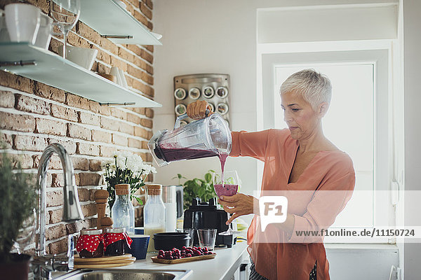 Older Caucasian woman pouring smoothie in kitchen