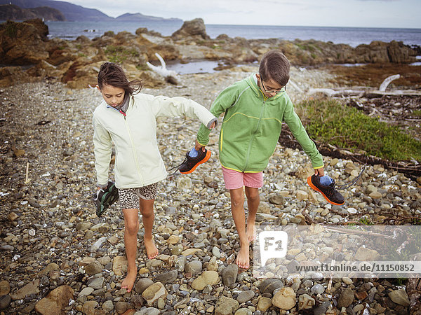 Mixed race brother and sister carrying their shoes on rocky beach