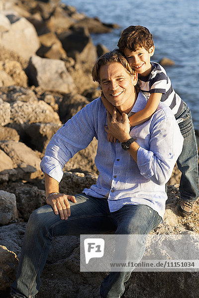 Caucasian father and son hugging on rocky beach