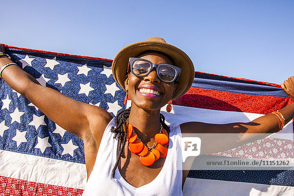 Schwarze Frau hält amerikanische Flagge unter blauem Himmel