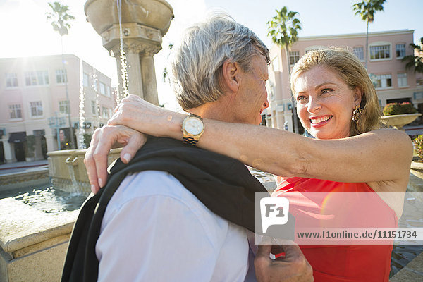 Older Caucasian couple hugging near fountain