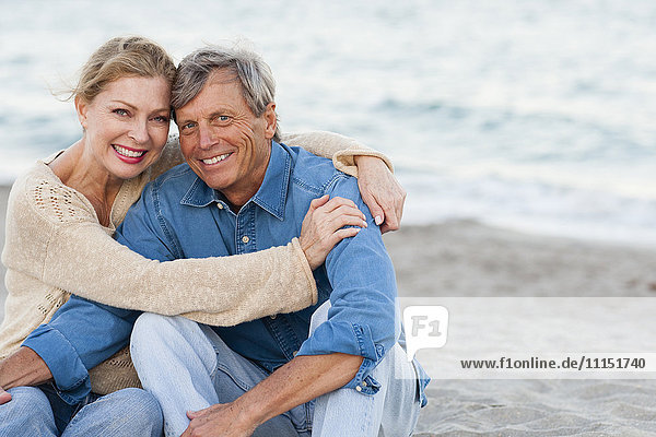 Older Caucasian couple hugging on beach