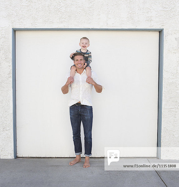 Caucasian father holding son on shoulders in driveway