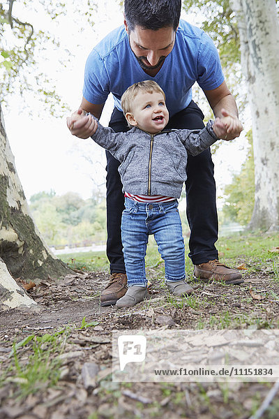 Kaukasischer Vater hilft seinem kleinen Sohn beim Laufen im Freien