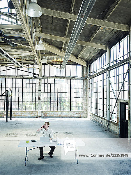 Caucasian businessman talking on cell phone in empty warehouse