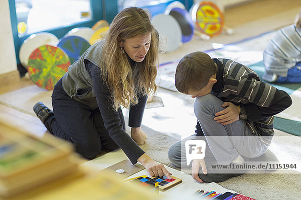 Caucasian Montessori teacher helping student in classroom