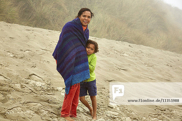 Gemischtrassige Mutter und Sohn umarmen sich am Strand