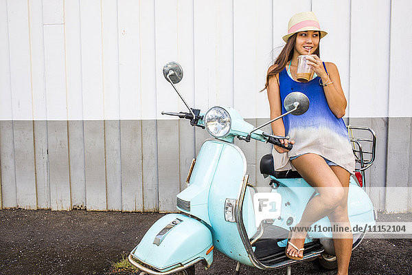 Pacific Islander woman drinking iced coffee on scooter