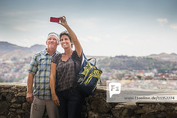 Caucasian couple taking cell phone photograph together on rooftop