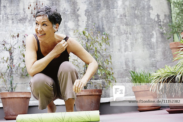 Ältere kaukasische Frau rollt Yogamatte im Innenhof auf