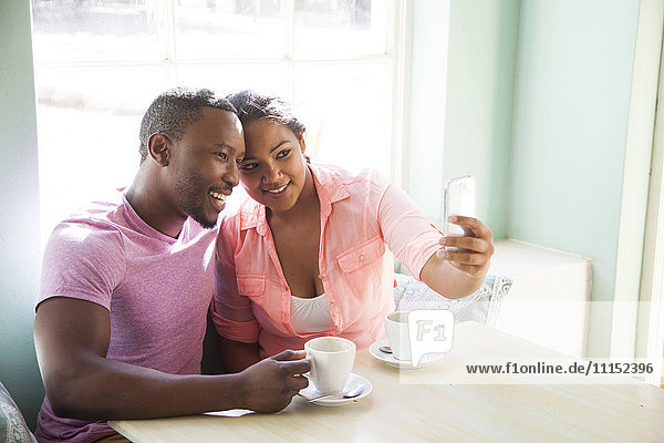 Smiling couple taking cell phone selfie at table with coffee