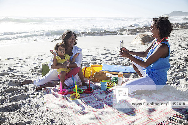 Mixed race mother photographing grandmother and daughter at beach