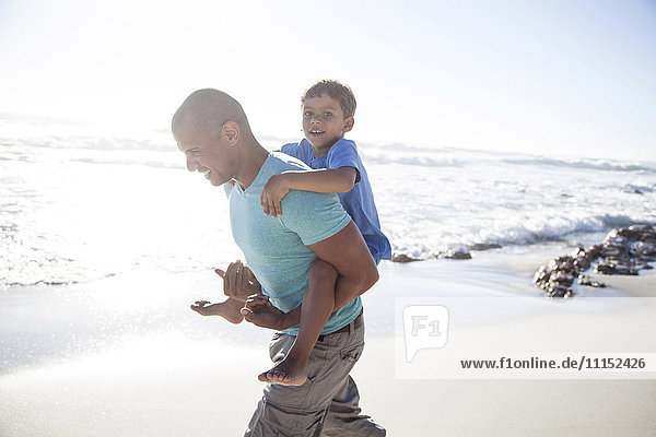 Gemischtrassiger Vater trägt Sohn huckepack am Strand