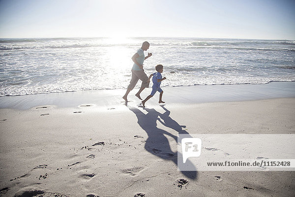 Gemischtrassiger Vater und Sohn laufen am Strand
