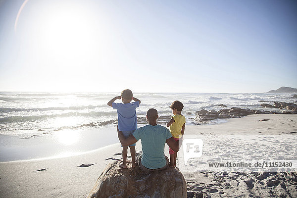 Mixed race father and children sitting on beach