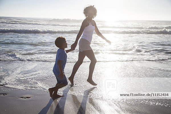 Mixed race mother and son playing in ocean waves on beach