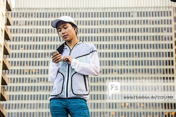 Asian runner using cell phone near highrise building