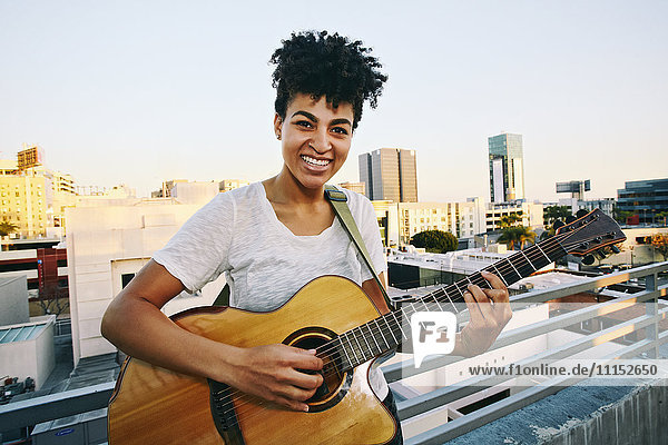 Lächelnde Frau  die auf einem Hausdach Gitarre spielt