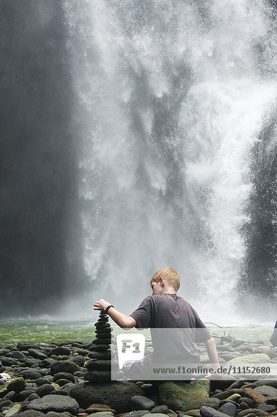 Kaukasischer Junge stapelt Steine in der Nähe eines Wasserfalls