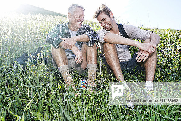 Kaukasischer Vater und Sohn sitzen auf einem grasbewachsenen Hügel