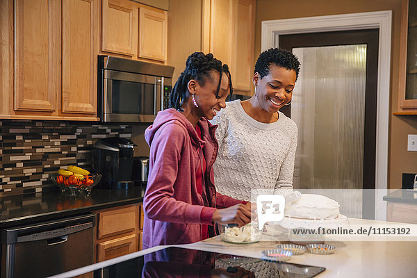 Black mother and daughter decorating cake in kitchen