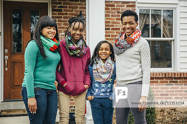 Schwarze Mutter und Töchter lächelnd vor dem Haus