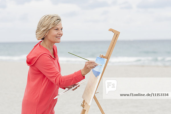 Ältere kaukasische Frau malt am Strand
