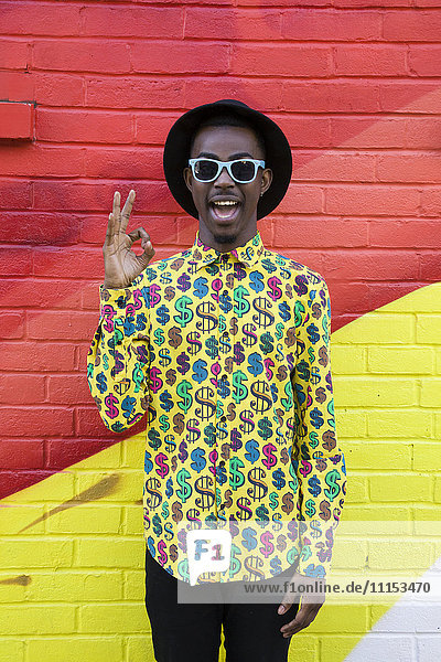 Black man in sunglasses making okay sign near colorful wall