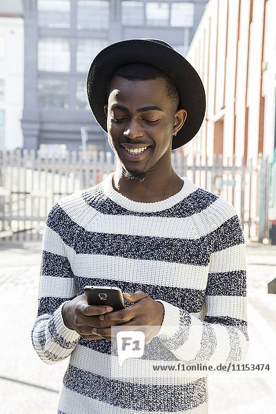 Schwarzer Mann benutzt Mobiltelefon auf städtischem Bürgersteig