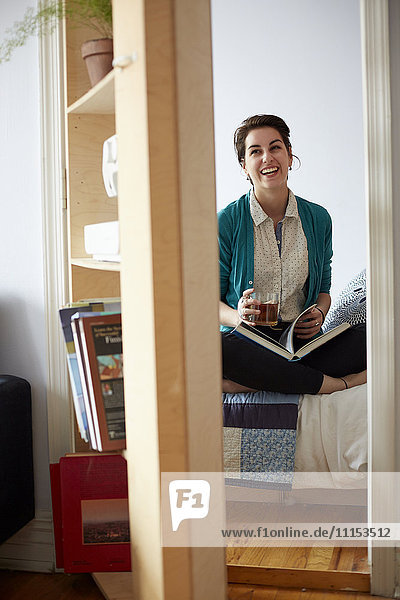 Woman drinking tea and reading in bedroom