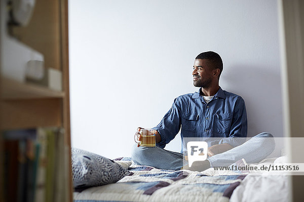 Black man drinking tea and reading on bed