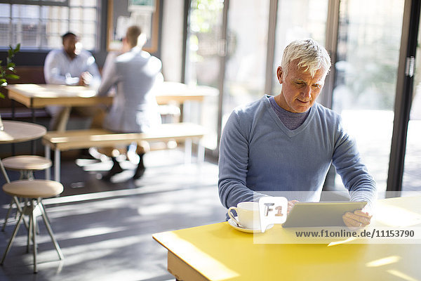 Älterer Mann benutzt digitales Tablet in einem Cafe