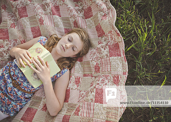 Kaukasisches Mädchen schlafend mit Buch auf Decke