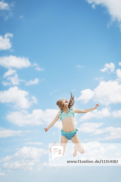 Kaukasisches Mädchen springt vor Freude in den blauen Himmel