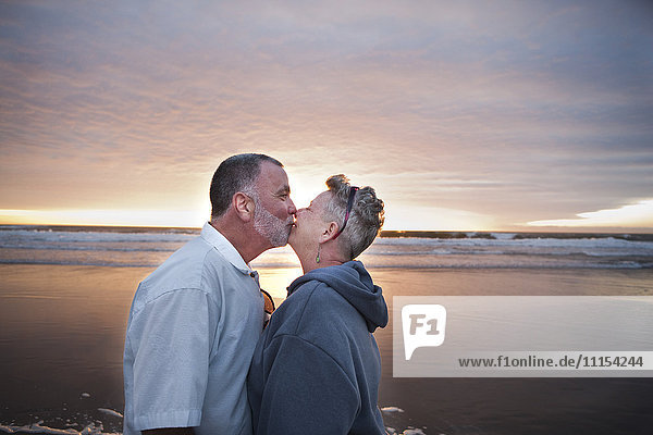 Caucasian couple kissing on beach at sunset