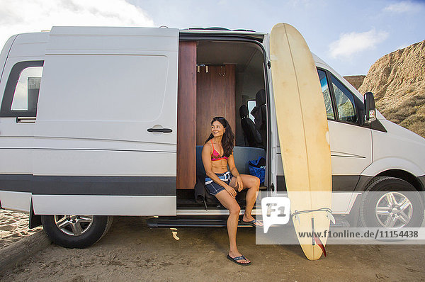 Hispanic surfer sitting in van with surfboard