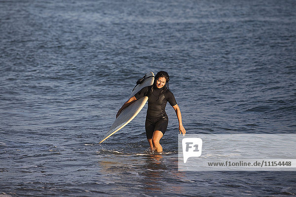 Hispanischer Surfer mit Surfbrett im Meer