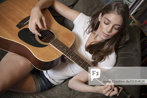 Caucasian woman playing guitar on sofa