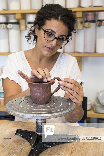 Frau platziert den Griff einer Tasse Ton in einer Keramikwerkstatt