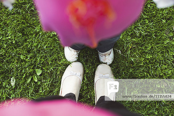 Hohe Winkelansicht der Füße von Mutter und Tochter im Gras