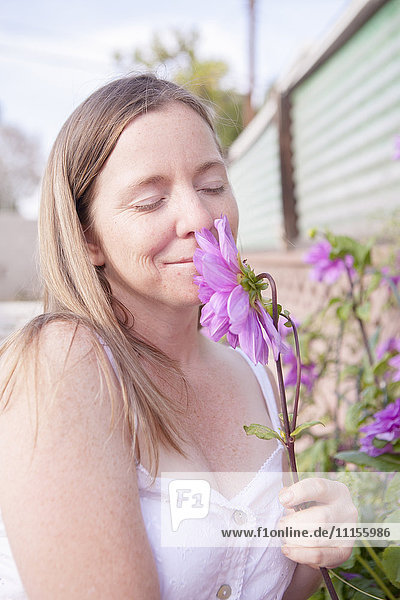 Gemischtrassige Frau riecht an Blumen im Garten