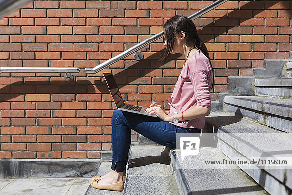 Woman sitting on stairs working with laptop
