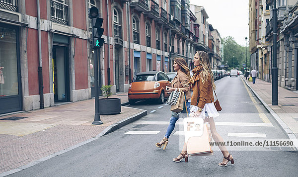Two women holding shopping bags crossing the street in the city
