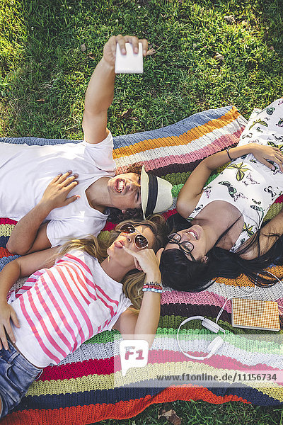 Verspielte Freunde  die auf einer Decke im Park liegen und einen Selfie nehmen.