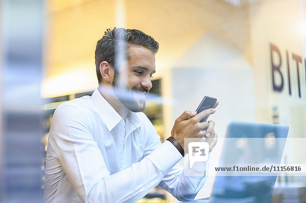 Lächelnder Geschäftsmann beim Anblick eines Handys in einem Café
