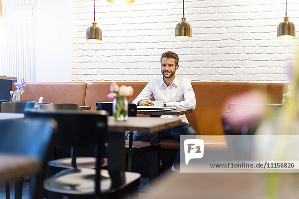 Lächelnder Geschäftsmann sitzend in einem Café mit einer Tasse Kaffee