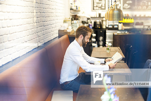 Geschäftsmann sitzt in einem Café und liest Zeitung.