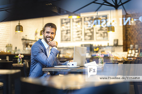 Lächelnder Geschäftsmann mit Laptop im Cafe